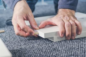 Man assembling furniture at home, male hand with wooden dowel pins and plywood board